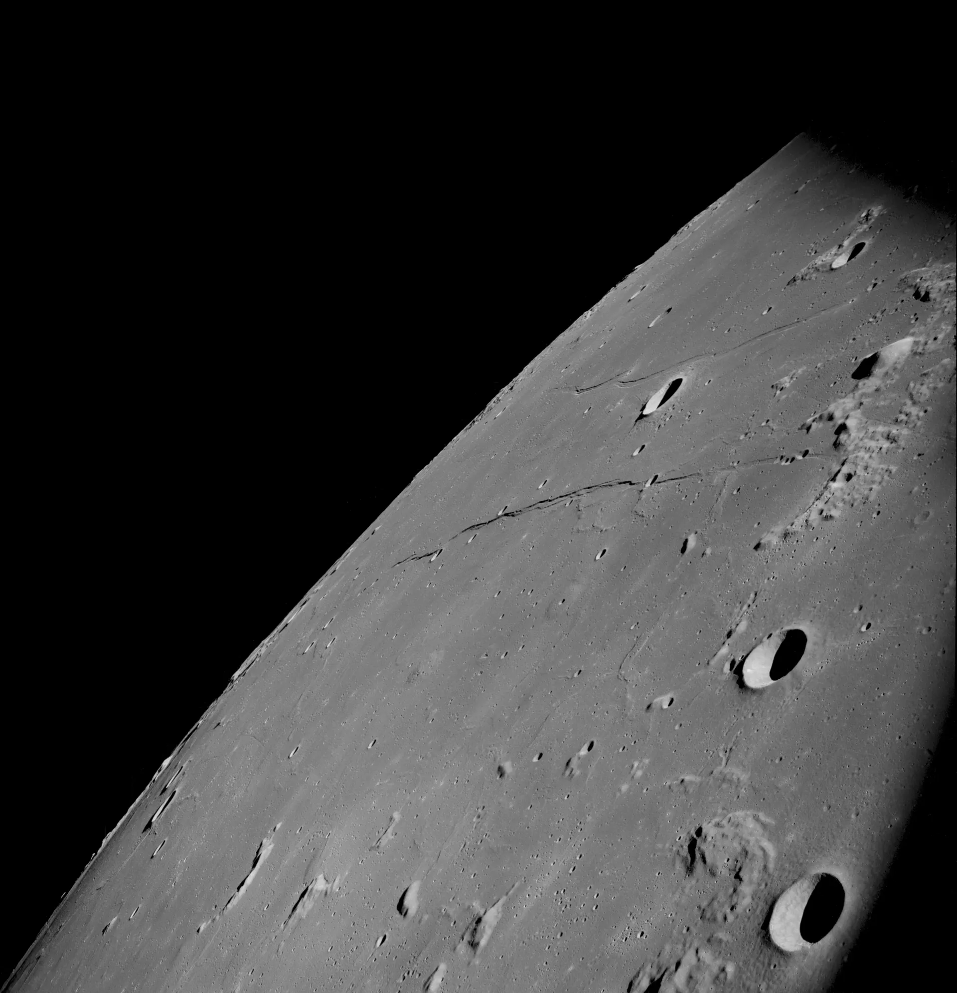 The cratered edge of the Moon’s Sea of Tranquility curving across the frame beneath a black sky, photographed from lunar orbit.