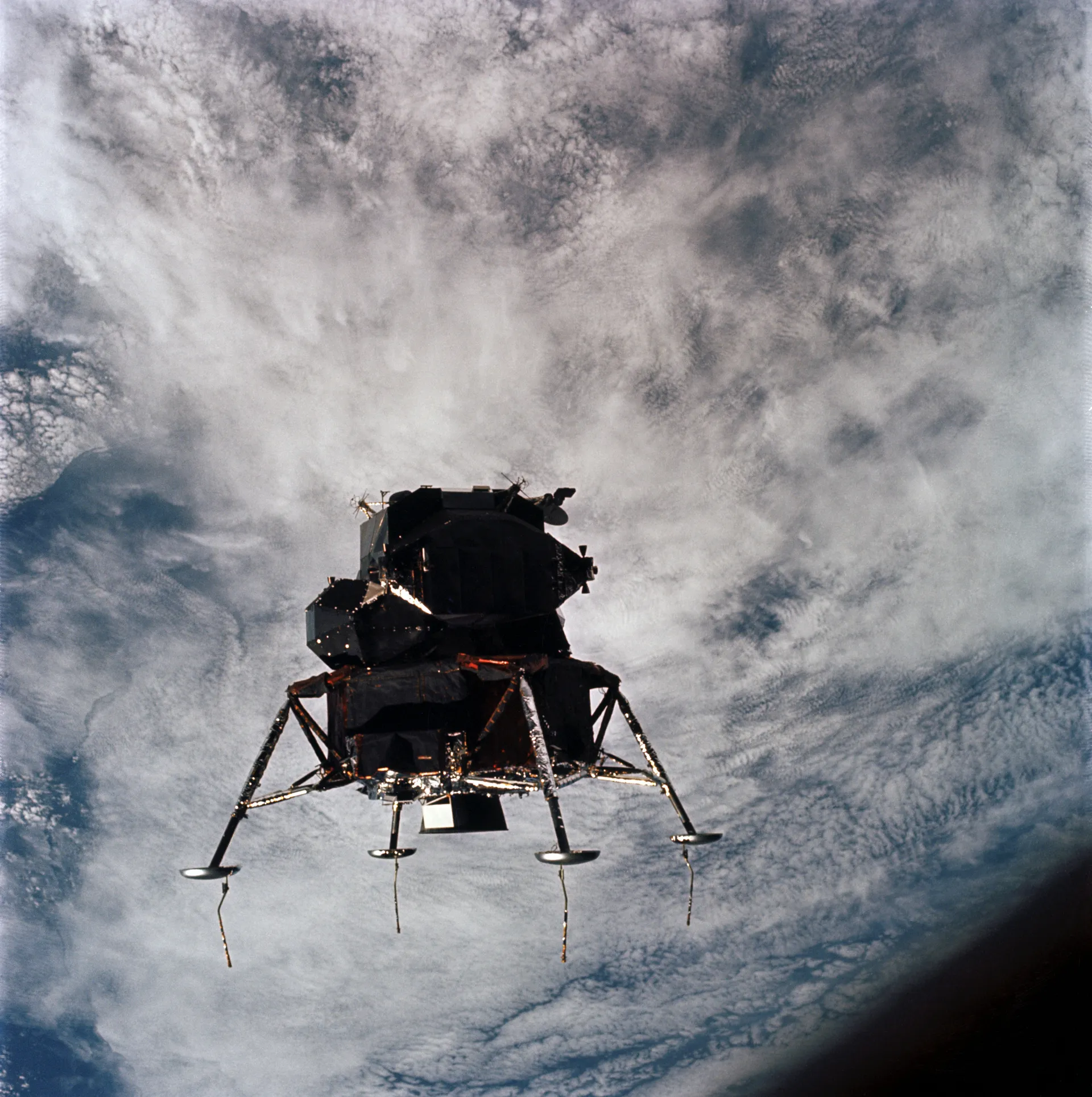 The Apollo 9 lunar module Spider in Earth orbit with its legs extended, over cloud-covered Earth.