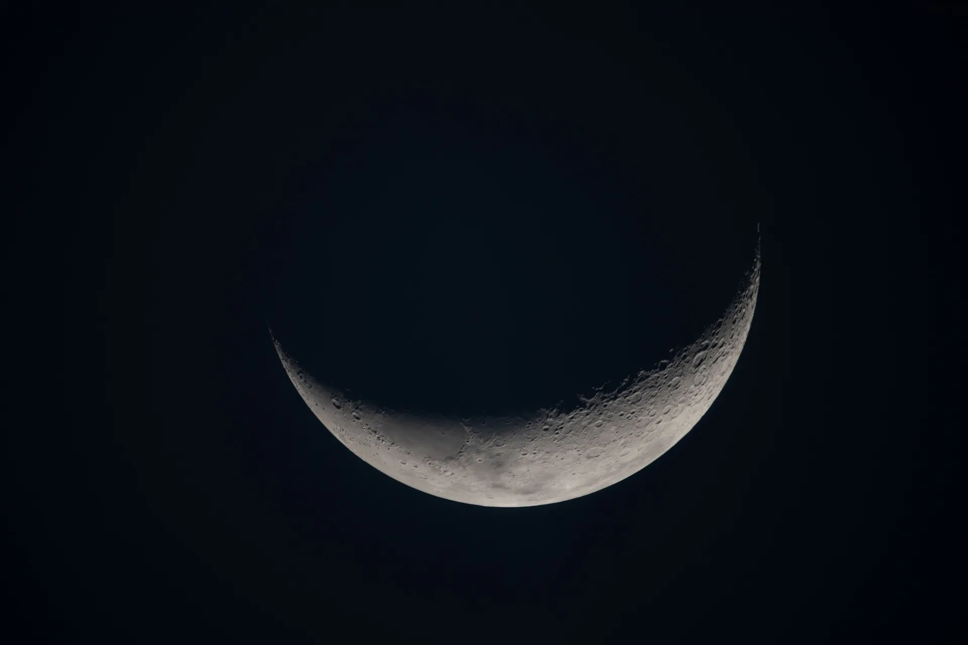 A thin crescent Moon against deep blue-black space, with craters visible along the terminator.
