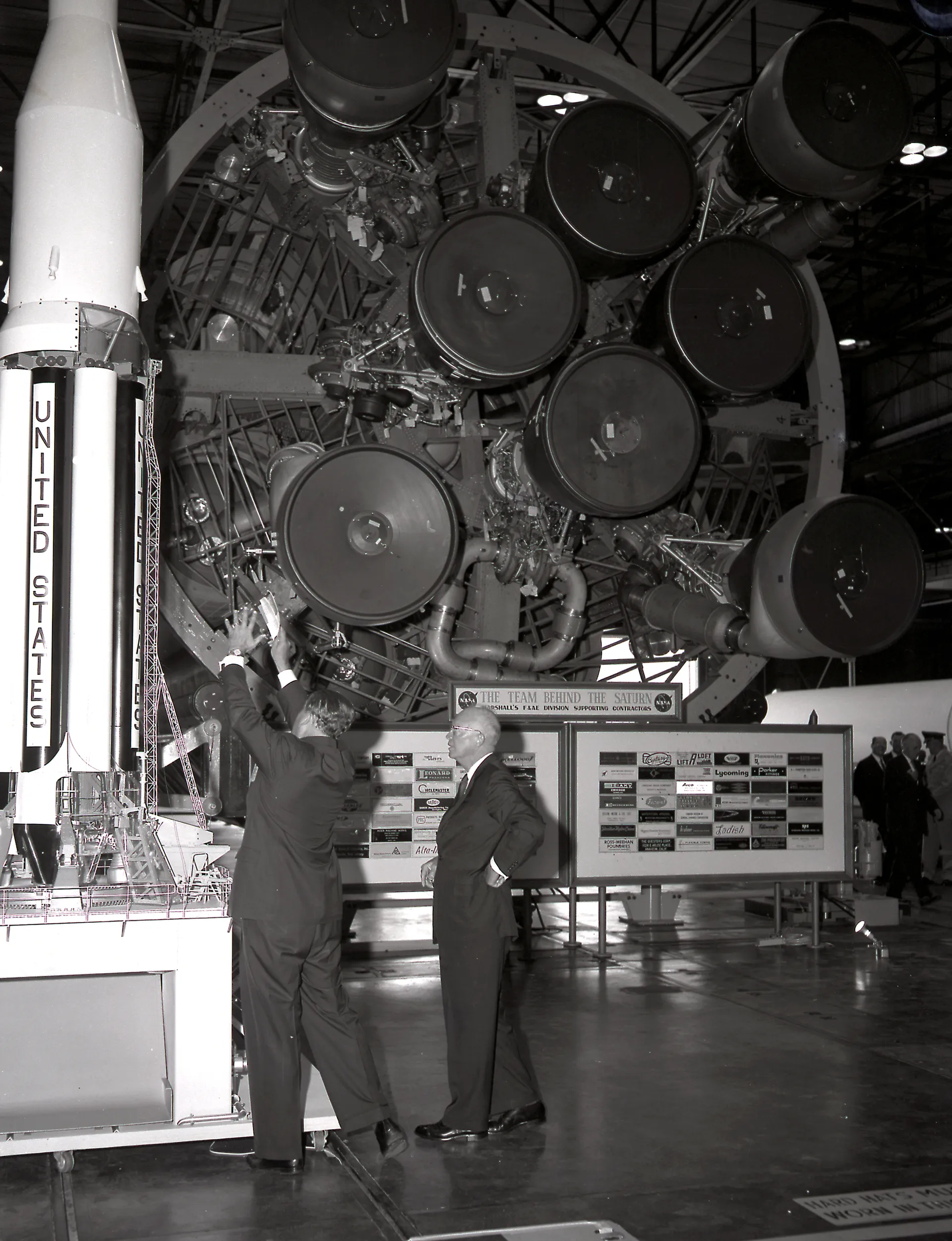 Wernher von Braun gestures toward the cluster of Saturn I engines above him while briefing President Eisenhower.
