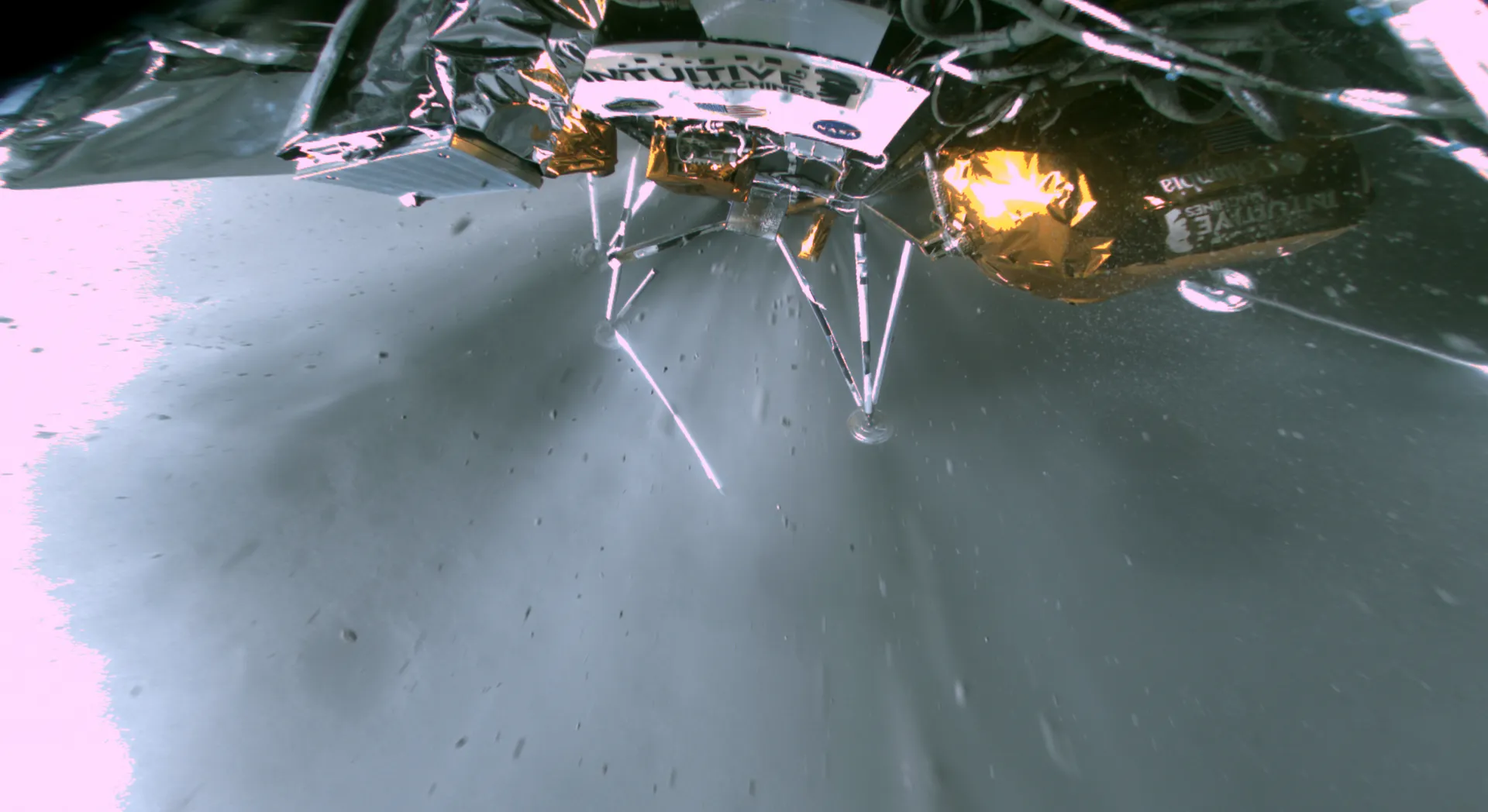 A wide-angle view from the lander shows its legs and a foil-covered tank above the gray lunar surface, dust flying outward.