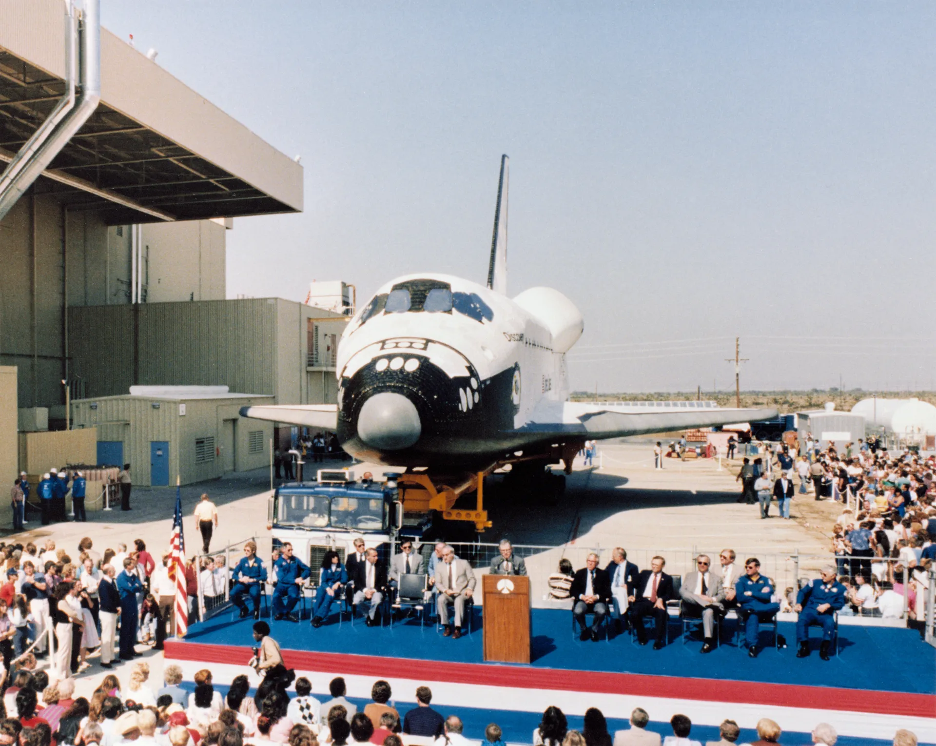 The orbiter Discovery stands behind a stage and seated crowd at its rollout ceremony.