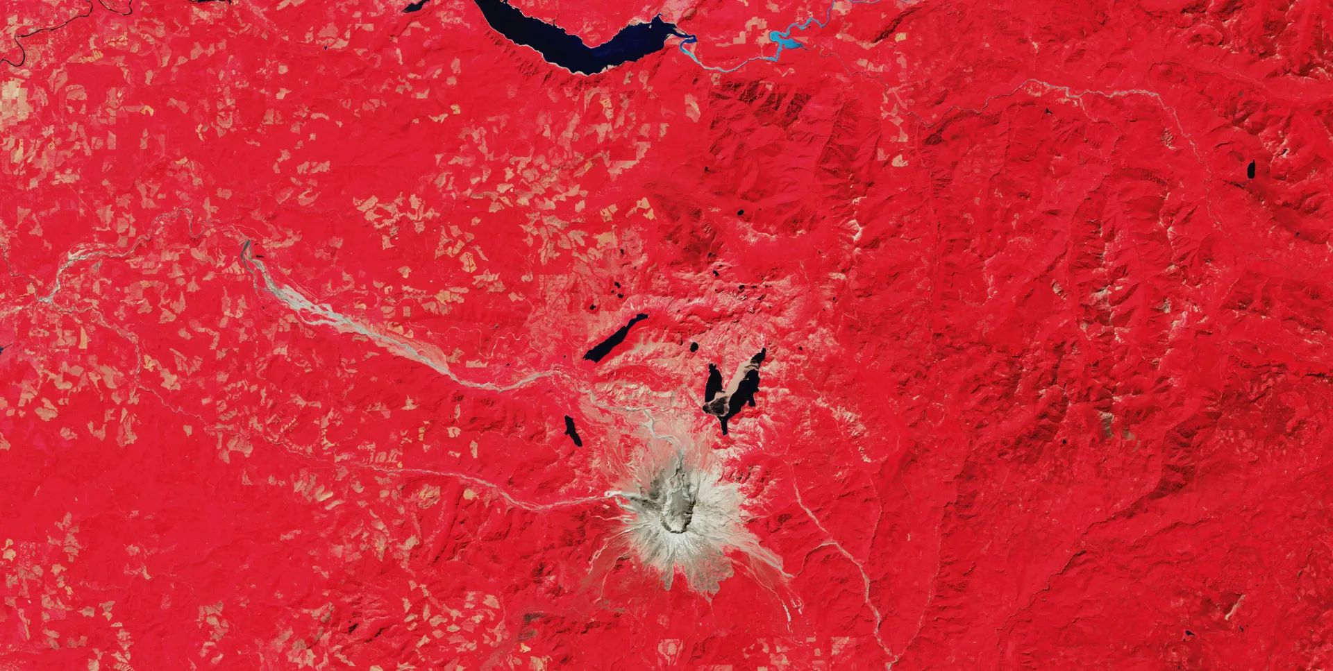 The same area in 2025: red vegetation has returned across most of the blast zone, leaving a smaller gray area around the crater.