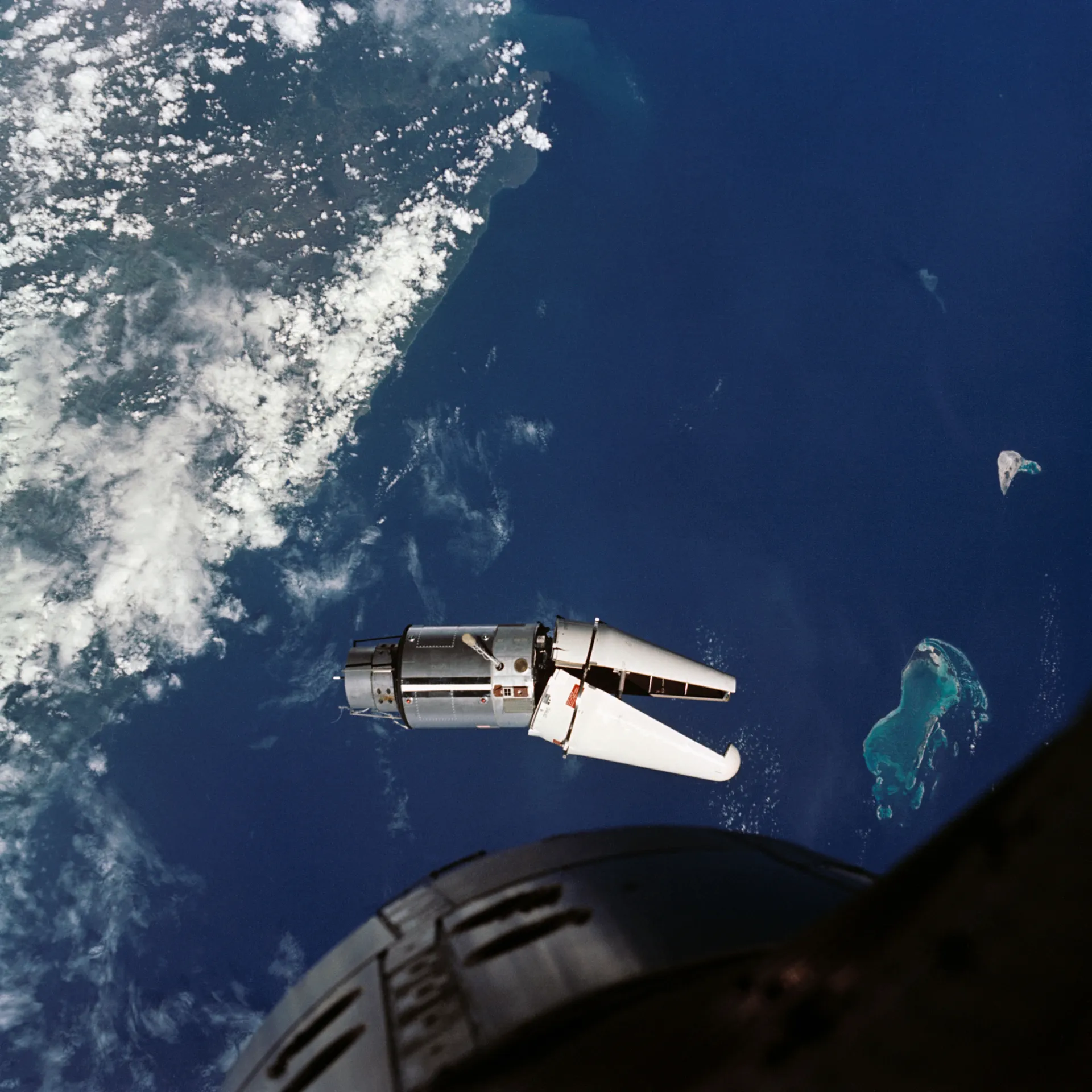 The Gemini 9A target adapter over the ocean, its nose shroud stuck half open like a jaw.