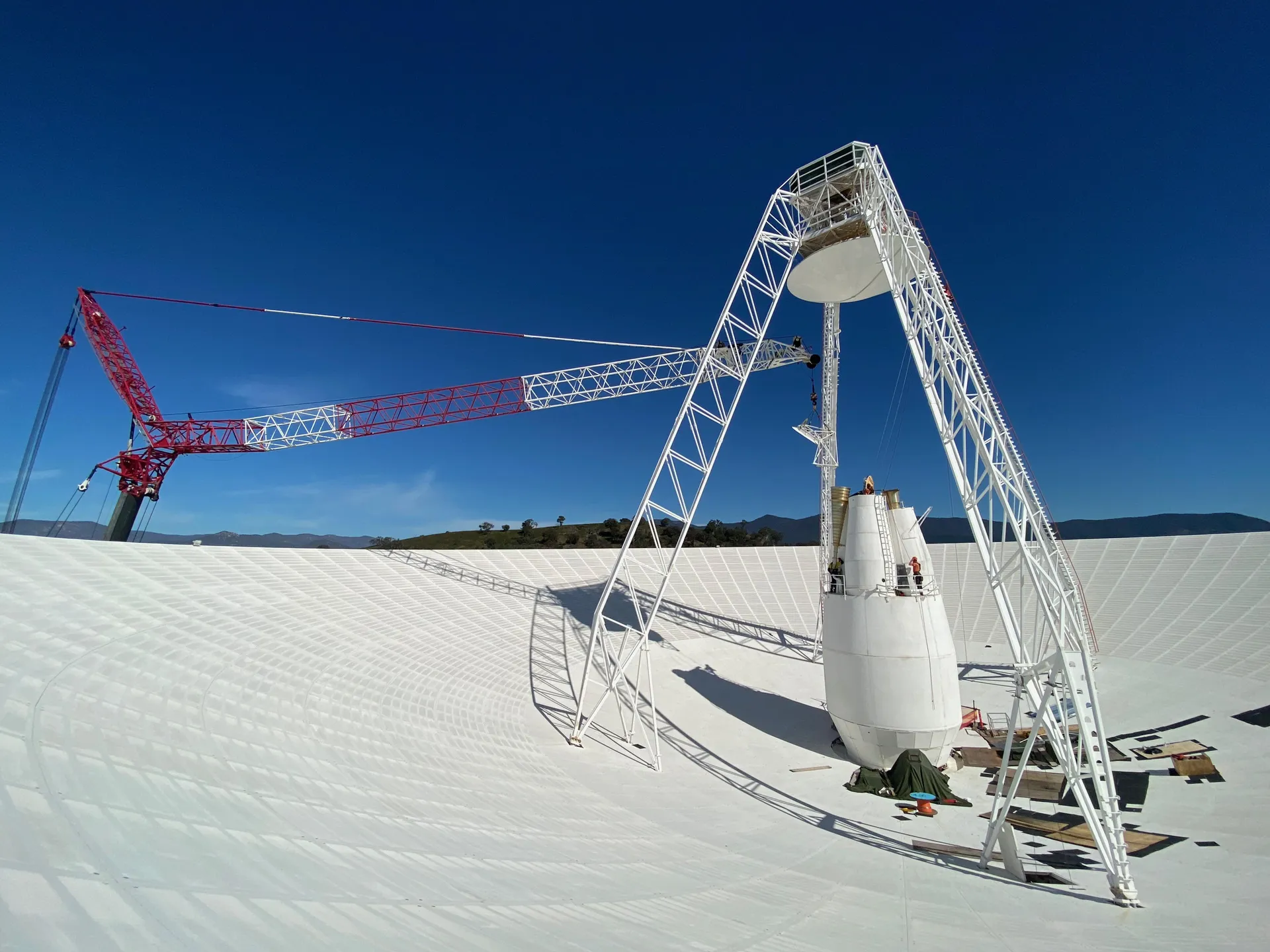 Workers on a lift are dwarfed by the white 70-meter dish of DSS-43 at Canberra, seen from inside the bowl.