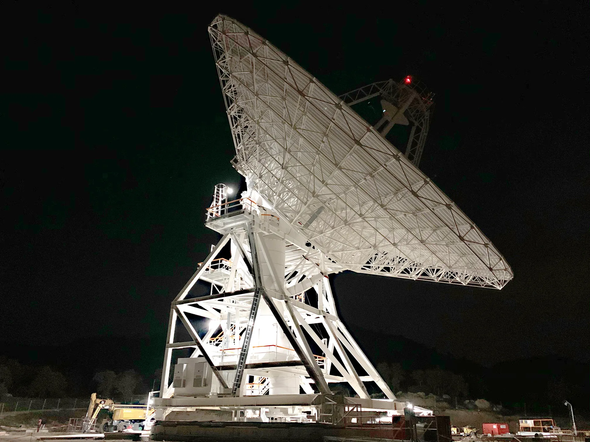 A 34-meter dish antenna at the Deep Space Network’s Madrid complex, lit against a black night sky.