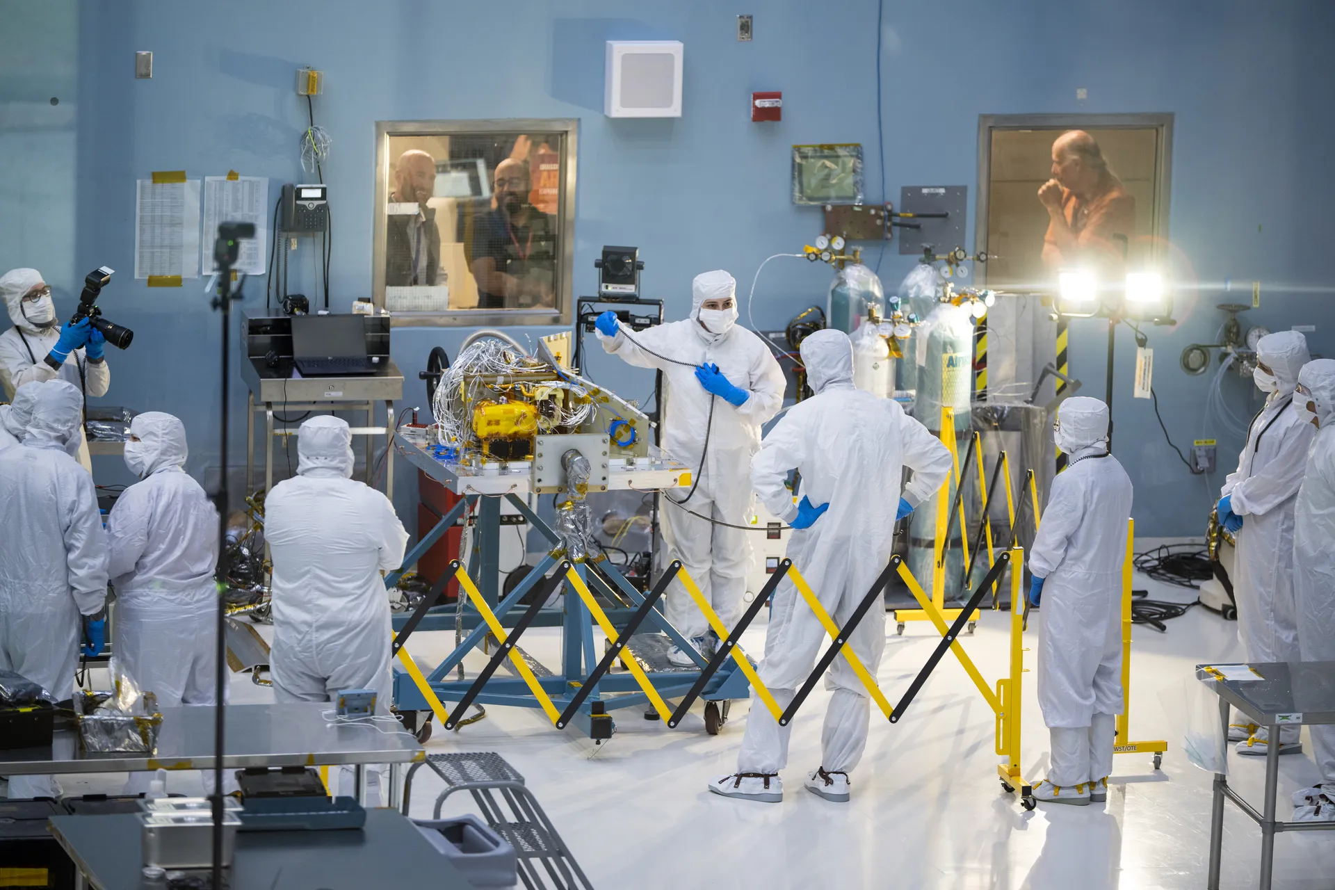 Engineers in clean-room suits work around the Dragonfly mass spectrometer on a stand at Goddard.
