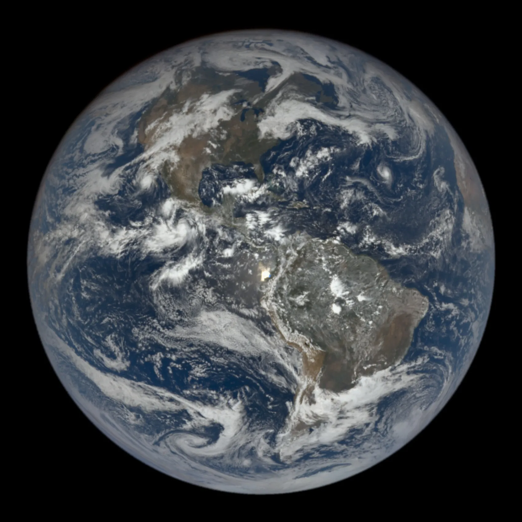 The fully lit disk of Earth against black space, showing North and South America under swirls of cloud.
