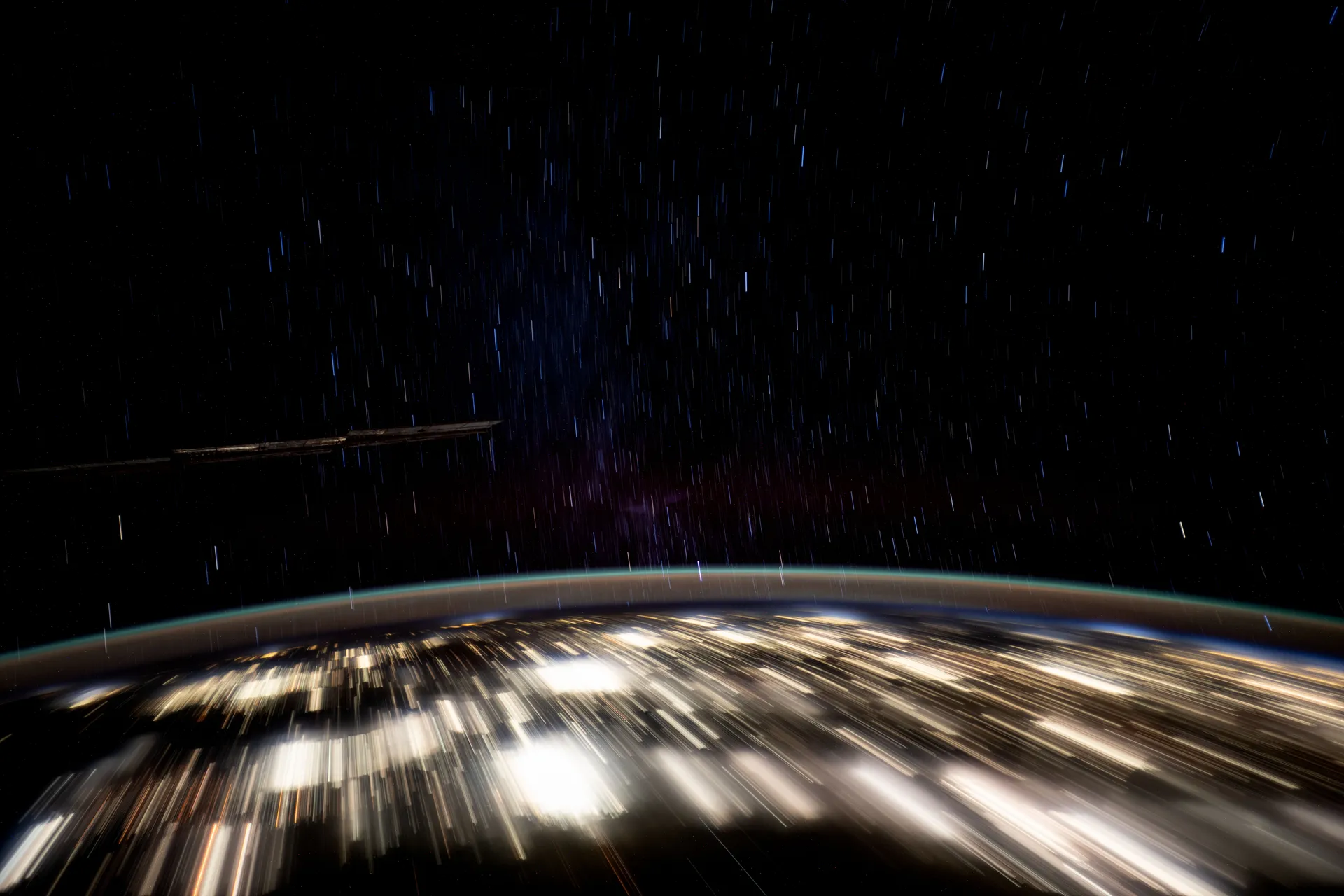 A long exposure from the space station: the city lights of the Yucatán peninsula smear into bright streaks below a thin band of atmosphere, with short star trails in the black sky above.