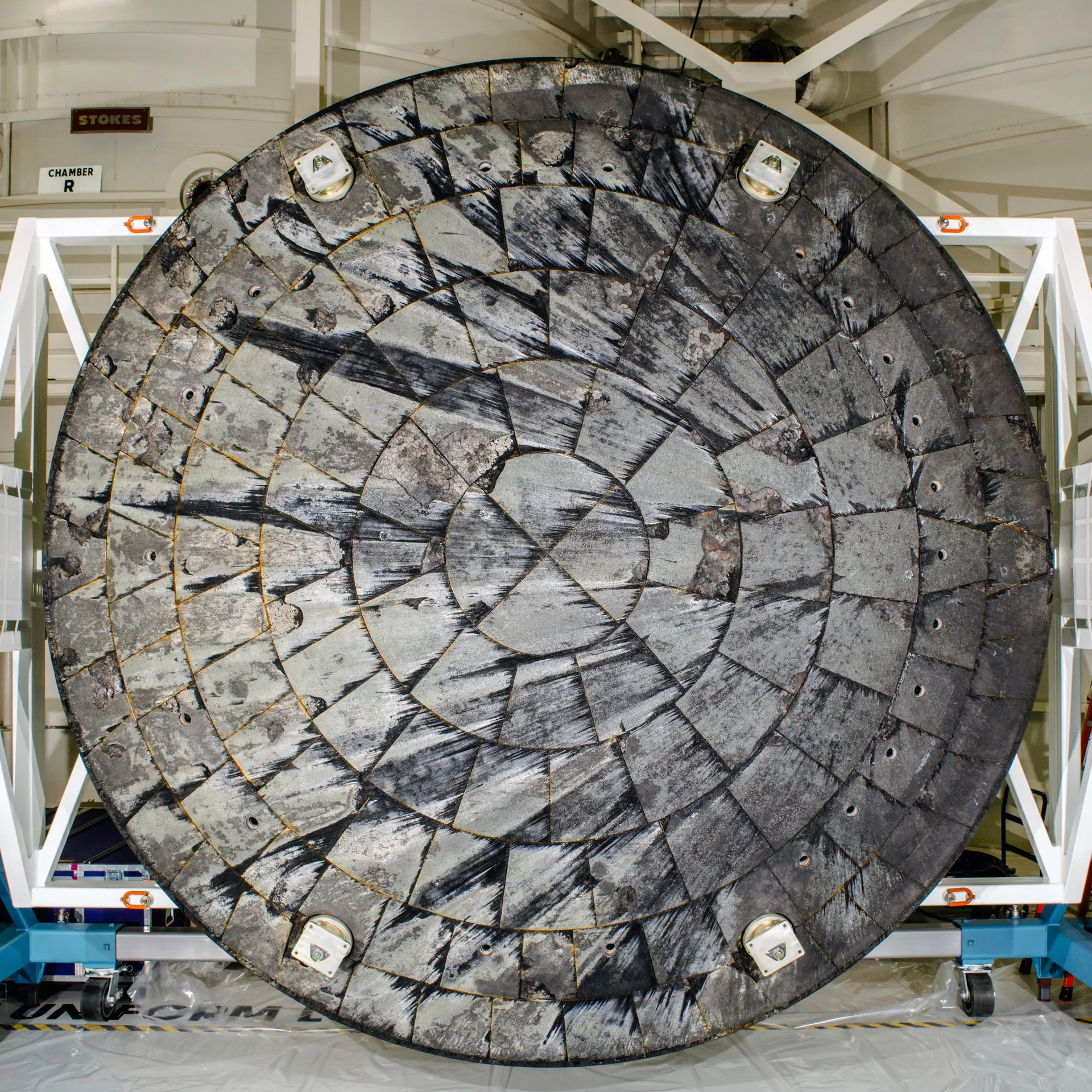 The Artemis I heat shield, removed from the capsule and standing on edge in a blue frame, its blackened surface crossed by cracks and dark patches.