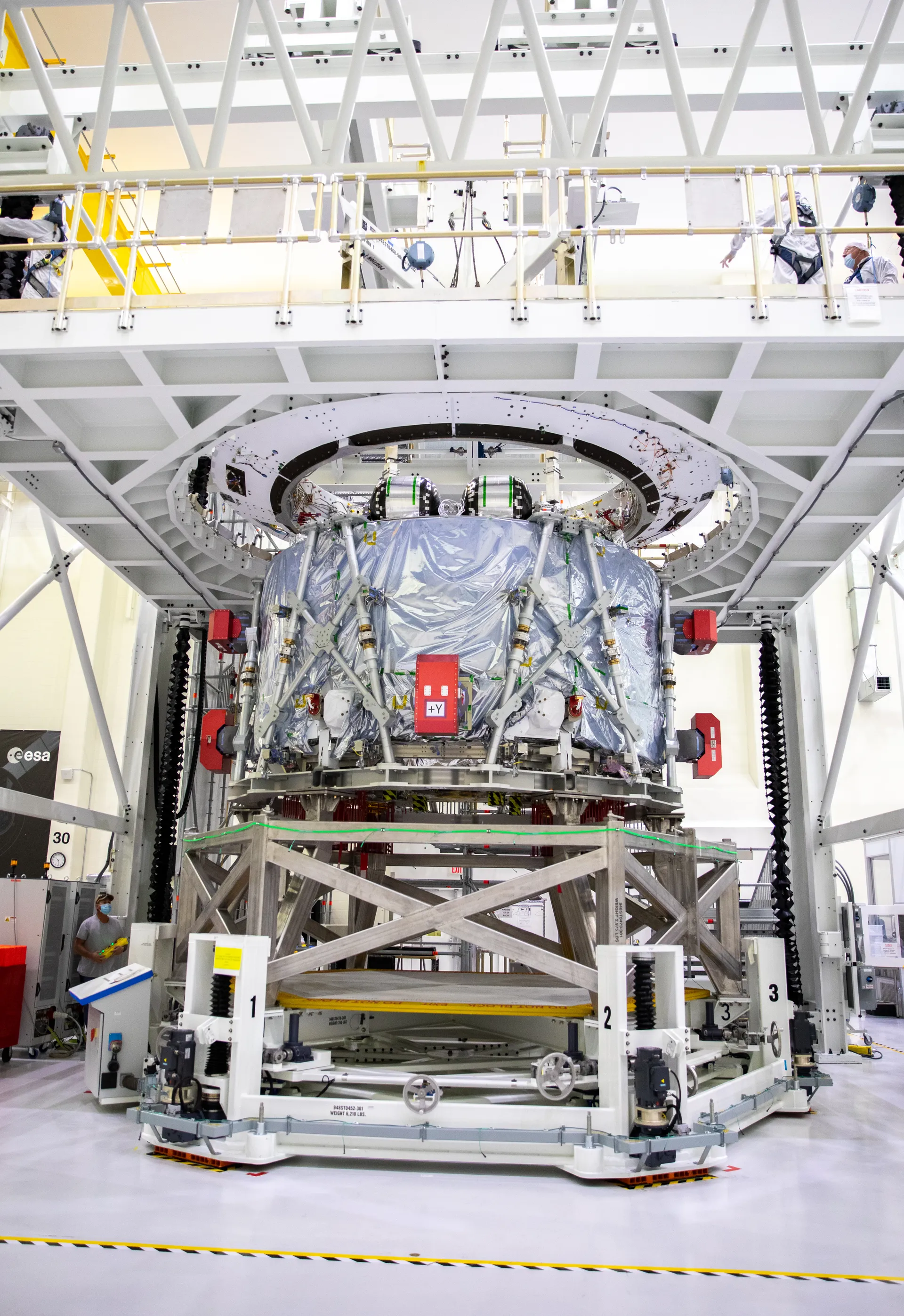 The European Service Module for Artemis II stands in a work stand in a high bay: a squat silver-wrapped cylinder with red protective covers.