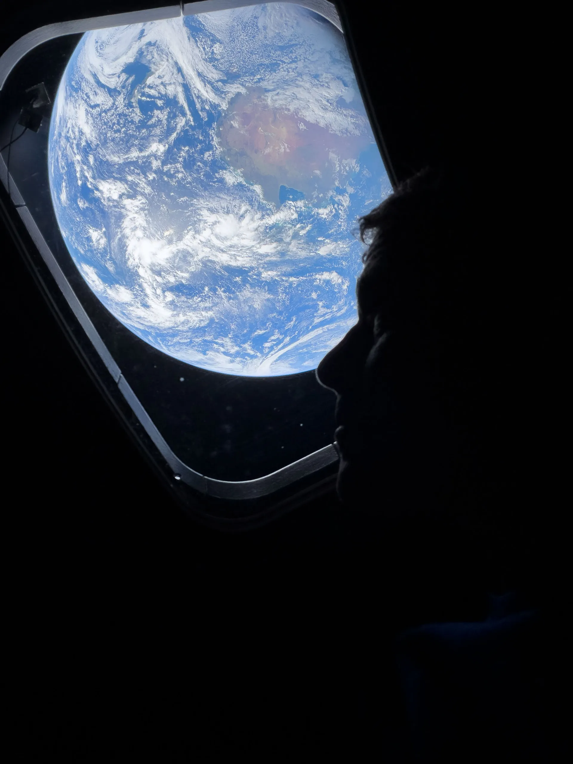 Reid Wiseman in silhouette at an Orion window, with a bright blue Earth filling the window.