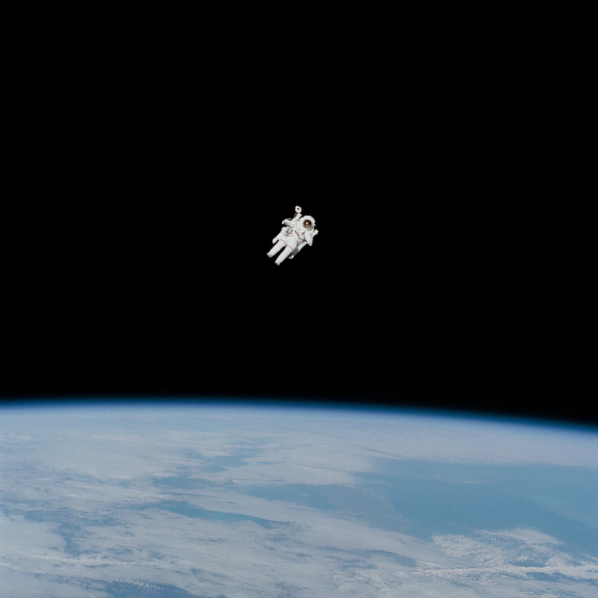 Bruce McCandless floats alone in black space on the Manned Maneuvering Unit, with Earth below.