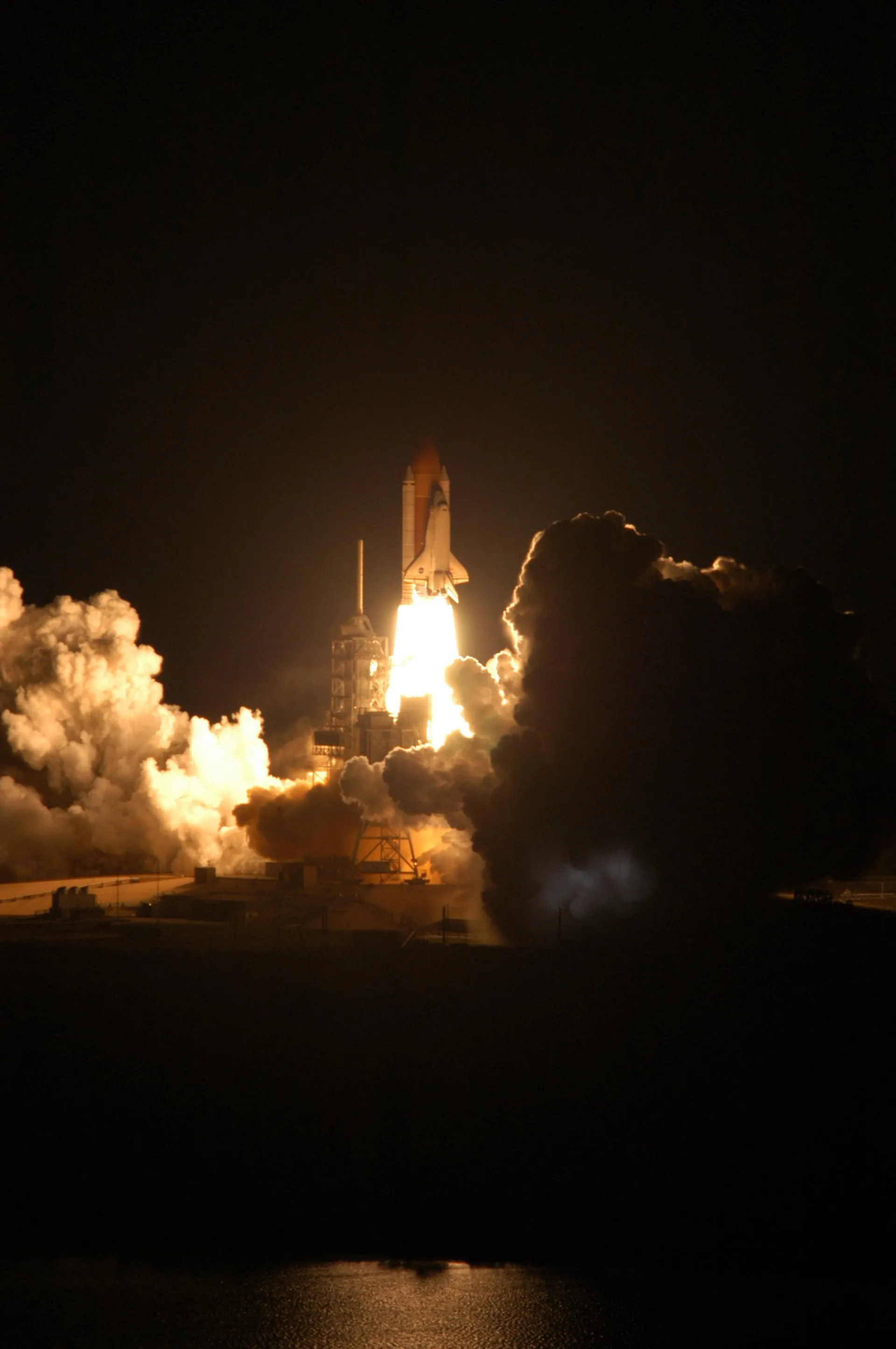 Discovery climbs from its pad at night on a pillar of fire, the external tank and two boosters lit beneath it.